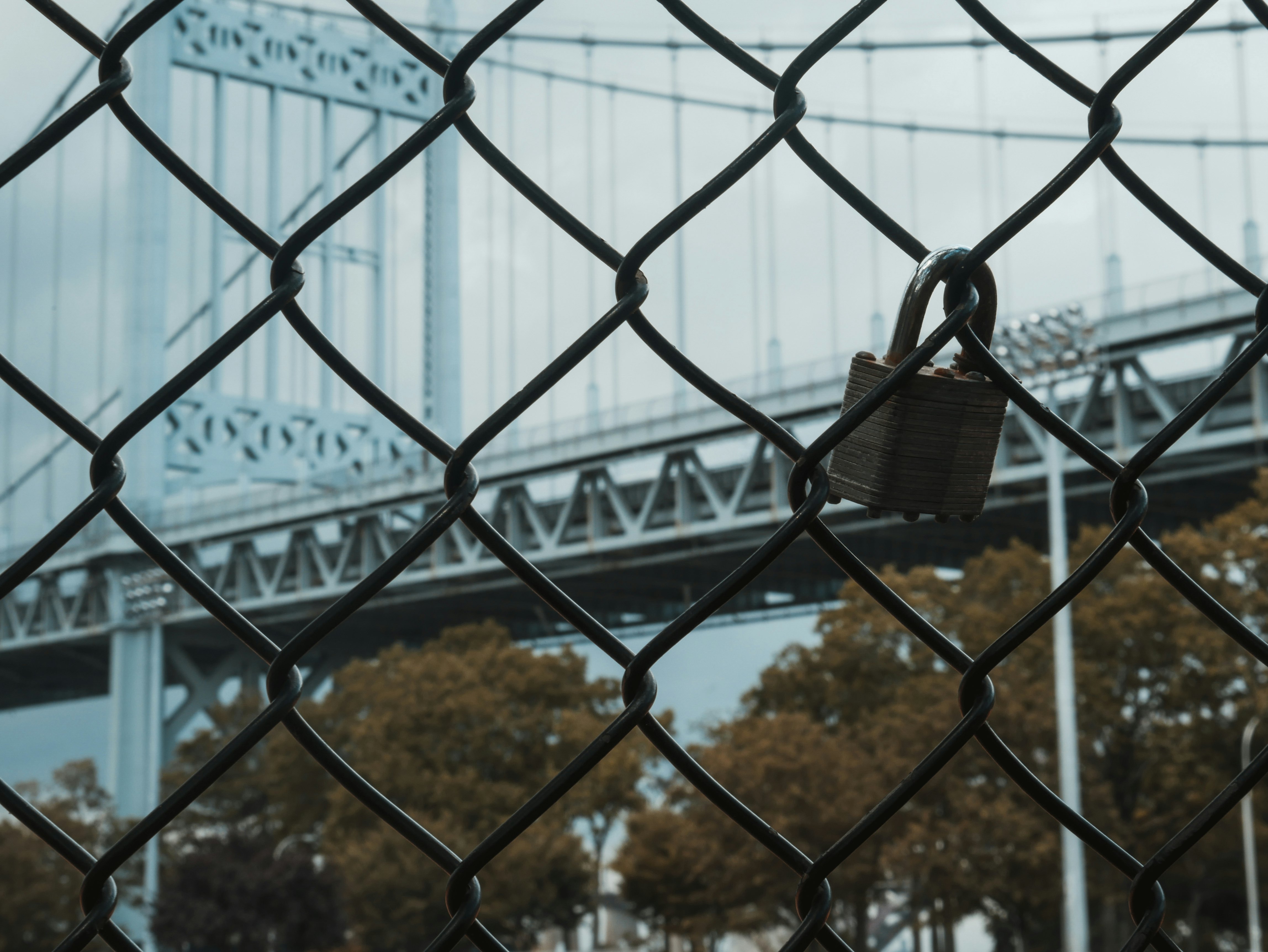Lock fastened to fence with bridge and trees in the background